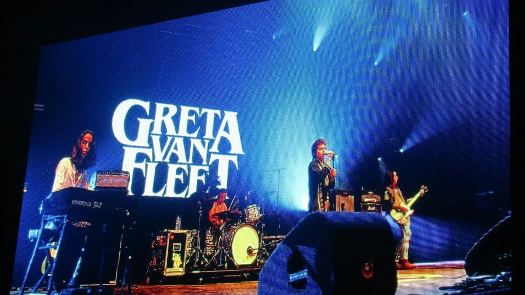 Greta Van Fleet performing on stage in front of their logo