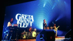 Greta Van Fleet performing on stage in front of their logo