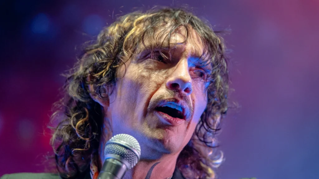 Justin Hawkins of The Darkness singing into a microphone under stage lights